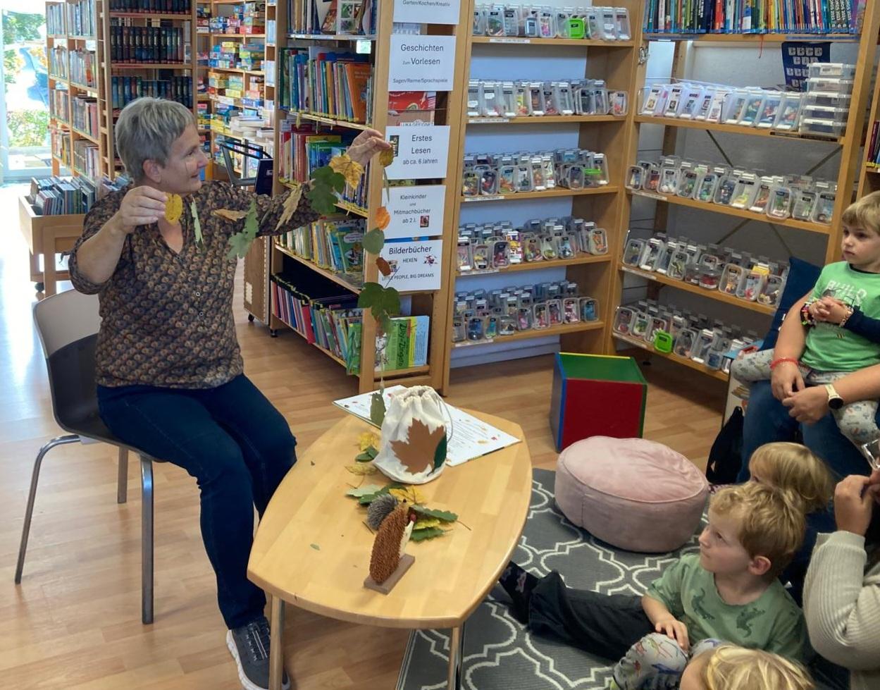 Frau hält eine Kette aus Blättern in Händen und zeigt sie Kindern