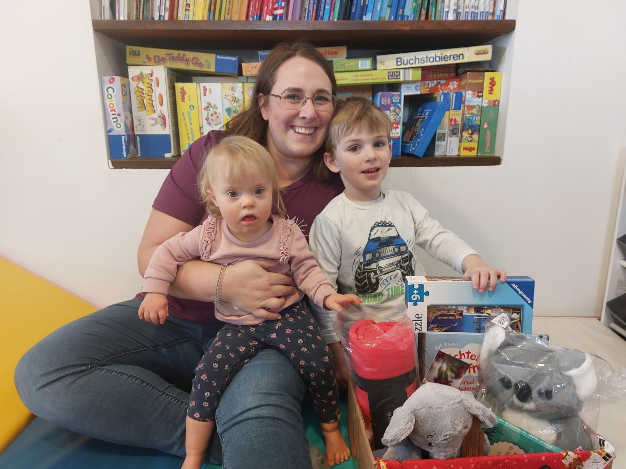 Frau mit zwei Kinder und Gewinn vom Schätzspiel lachen in die Kamera